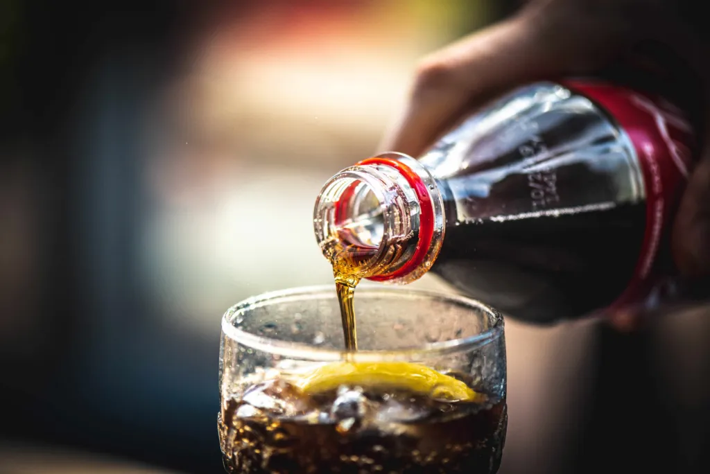 Refreshing beverage being poured into a clear glass filled with ice cubes and sliced fresh lemon